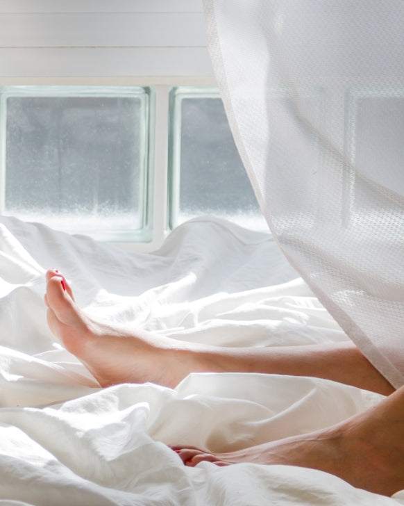 feet on bed poking through duvet, sunlit window in the background