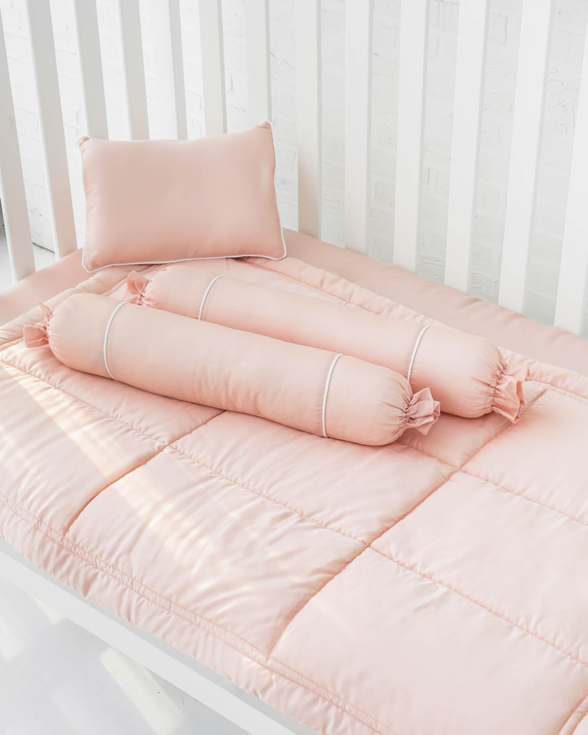 White crib with blush peach pink organic bamboo lyocell baby bedding (baby comforter set - 1 pillowcase, 2 bolstercases, 1 comforter; baby pillow set - 1 headshaping pillow, 2 bolsters; crib fitted sheet)