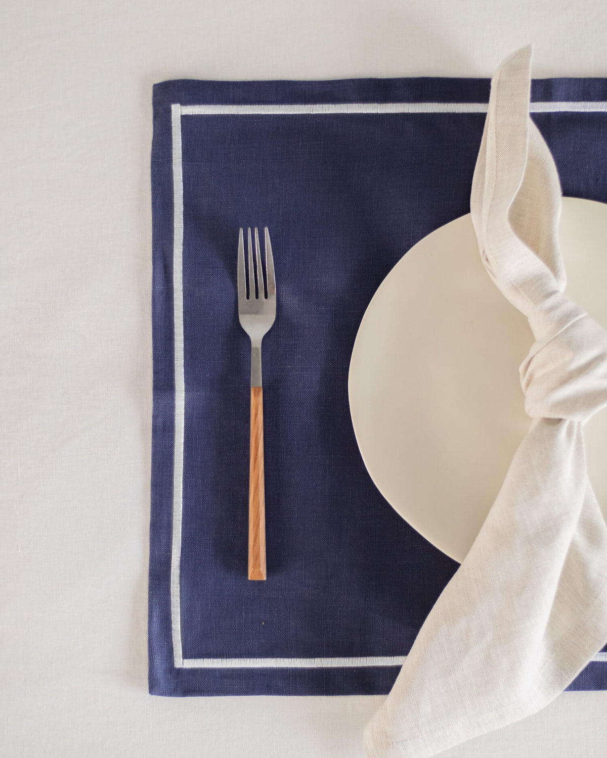 ava and ava Blue pure linen placemat with white embroidered border, with white linen napkin, white plate, silver wood cutlery