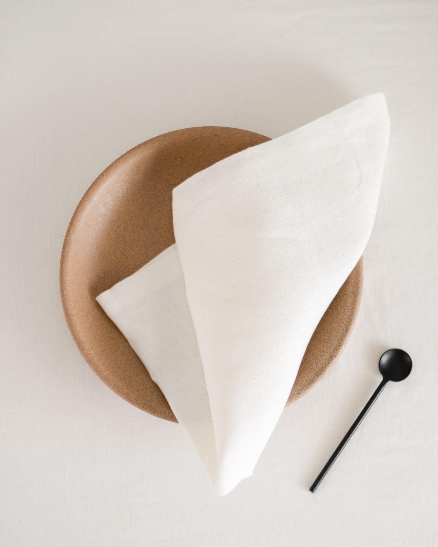 ava and ava White pure linen table napkin on white plate, knotted, with black dessert spoon