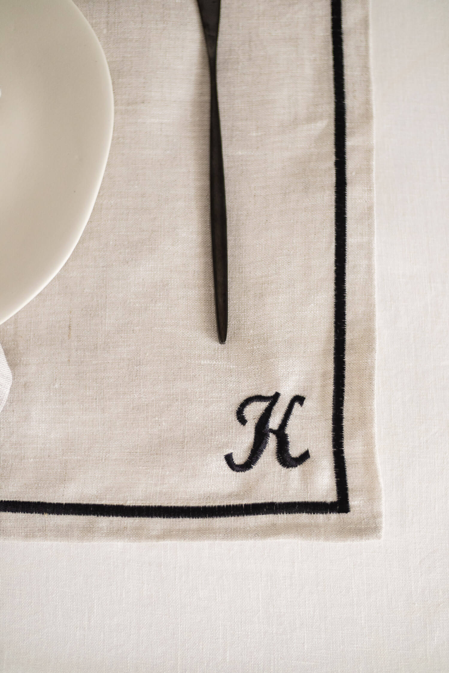 ava and ava natural pure linen placemat with black embroidered border, with white linen napkin, white plate, silver wood cutlery with custom embroidery monogrammed initials