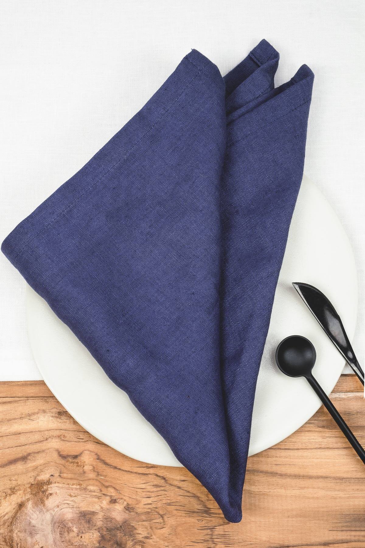 ava and ava Denim blue pure linen table napkin on white plate, with black cutlery