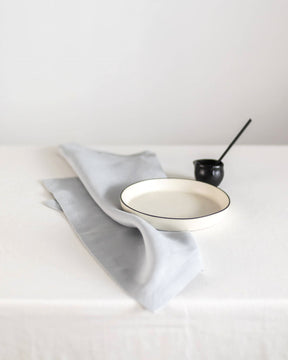 ava and ava ph Light gray pure linen table napkin on white plate, folded into triangle shape, with black dessert spoon