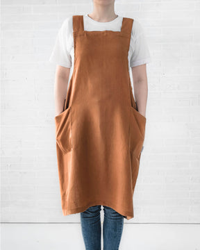 ava and ava ph caramel color pure linen crossback apron on female adult, hands on side pockets