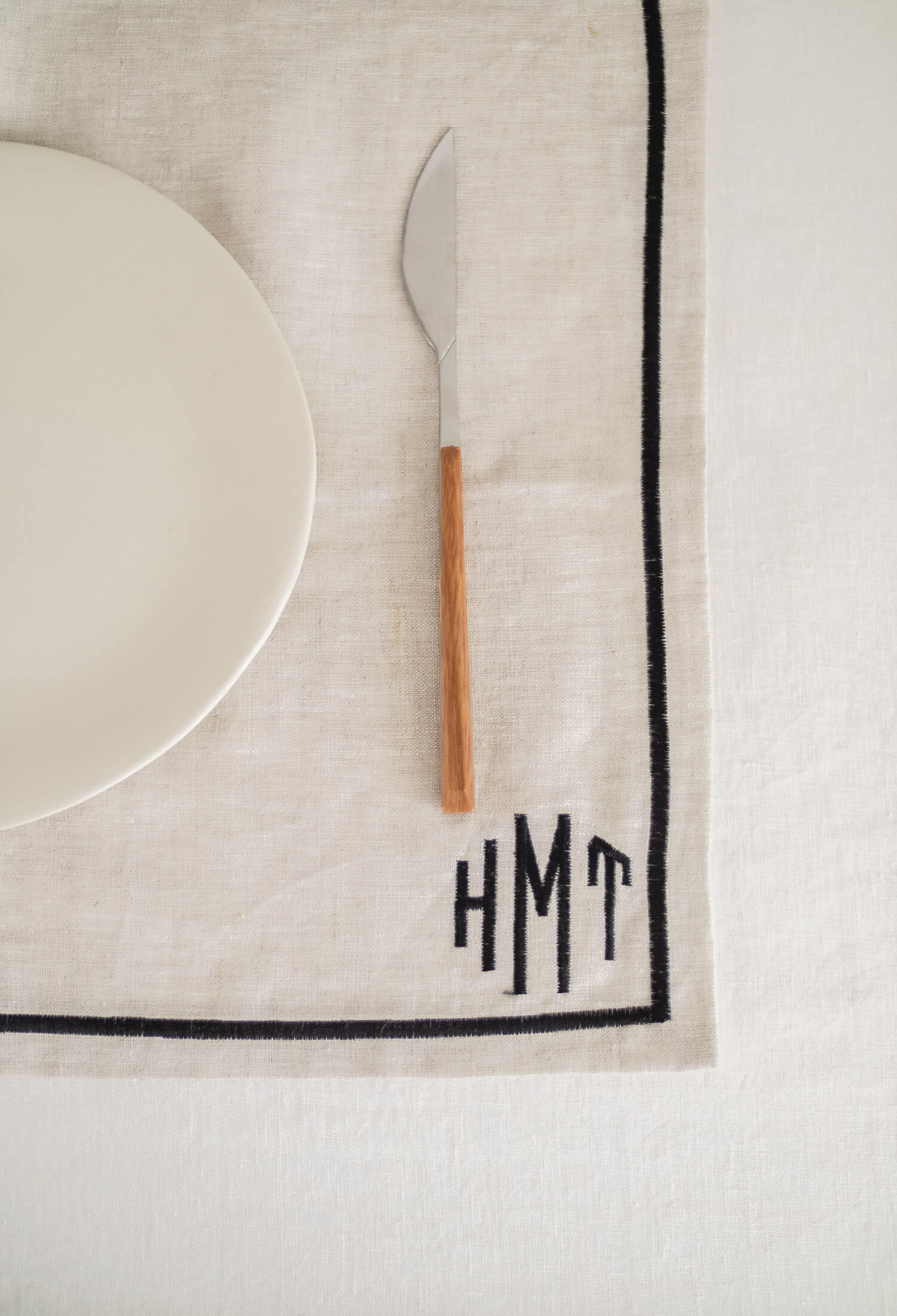 ava and ava natural pure linen placemat with black embroidered border, with white linen napkin, white plate, silver wood cutlery with custom embroidery monogrammed initials